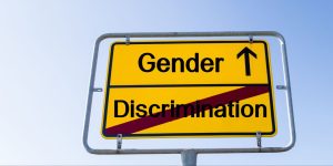 A road sign with the words gender discrimination with discrimination crossed out